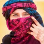 http://A%20woman%20in%20Merzouga,%20Morocco,%20wearing%20a%20colorful%20hijab%20and%20henna%20tattoo,%20standing%20in%20the%20desert.