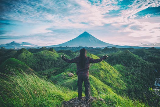 A person enjoys an expansive view of Mt. Mayon amidst lush green hills in Bicol, Philippines.